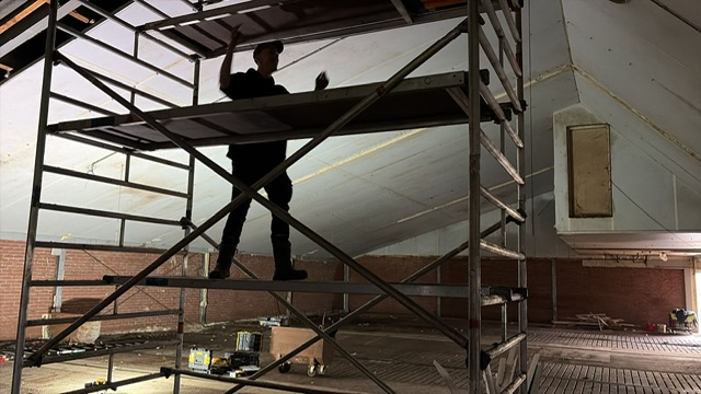 Vakman werkt vanaf een rolsteiger aan het dakvlak binnen een leeg pand
