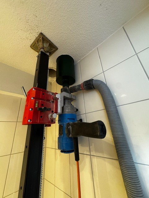 Kernboormachine op geleiderail boort met stofafzuiging een doorvoer in een betegelde ruimte