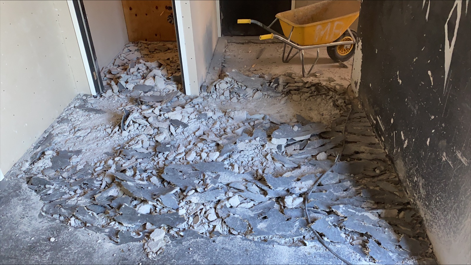 Verwijderde dekvloer en gesorteerd puin in een woning met een kruiwagen op de achtergrond