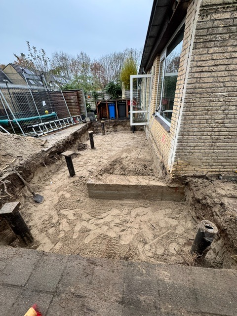 Vrijgegraven fundering langs een woning met zichtbare funderingspalen